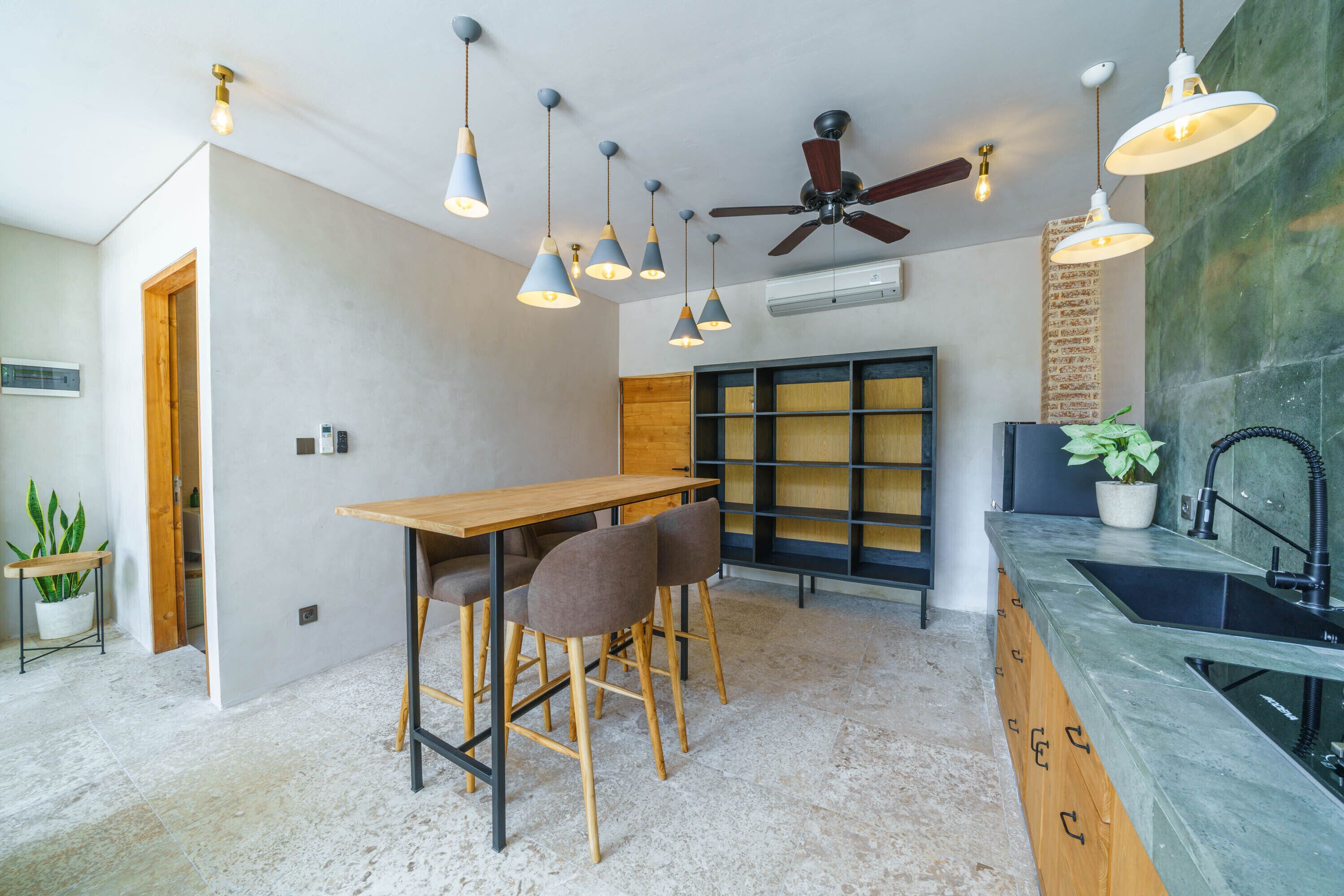 Cozinha moderna com mesa de madeira, banquetas, luminárias pendentes, ventilador de teto e pia embutida.