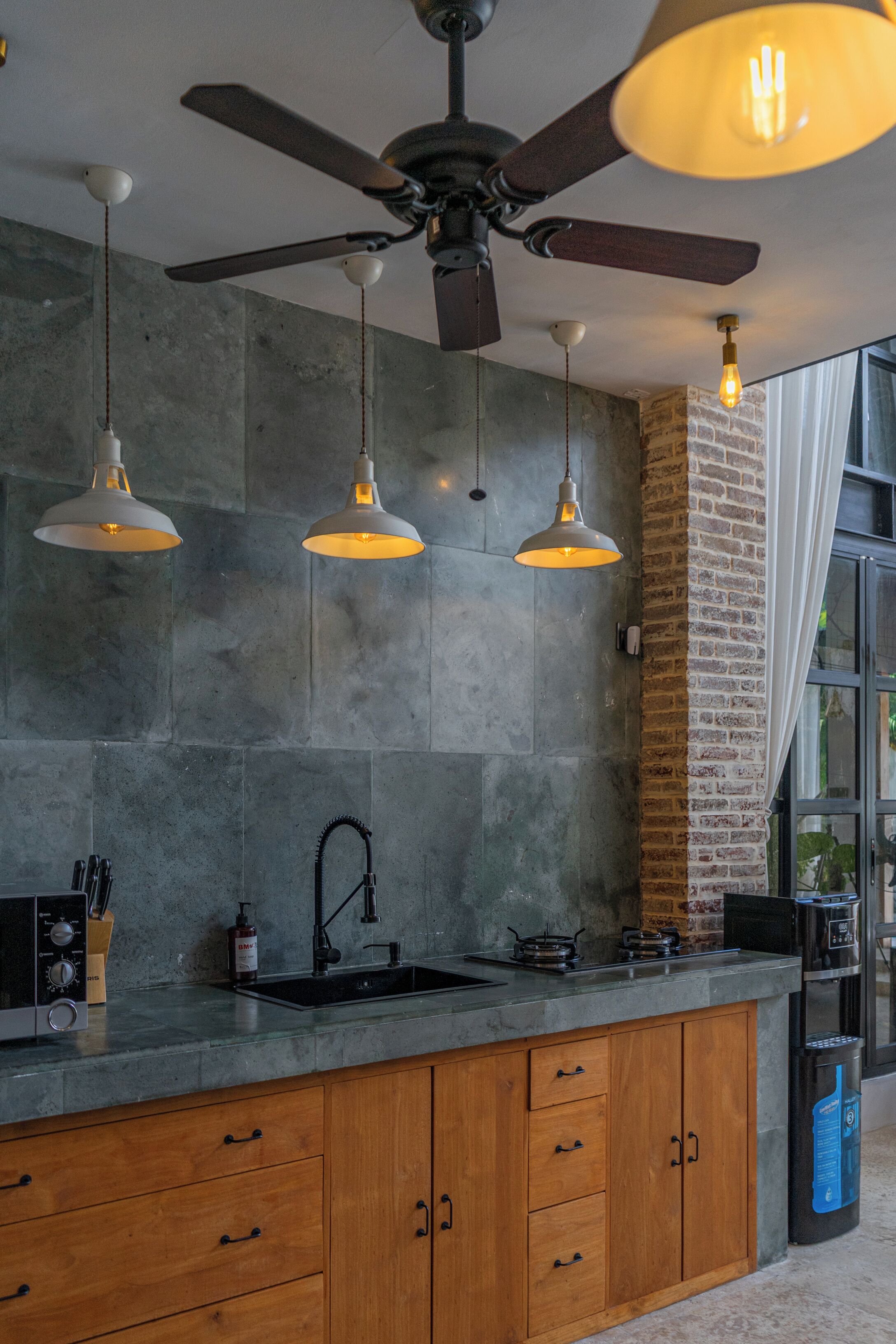 A kitchen with a modern design, featuring a large island with a sink, a ceiling fan, and pendant lights.
