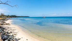 Una playa con agua turquesa cristalina, una orilla arenosa y un velero a lo lejos.