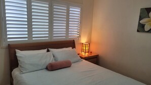 Una cama bien hecha con almohadas blancas y estampadas, un cabecero de madera y una mesita de noche con una lámpara.