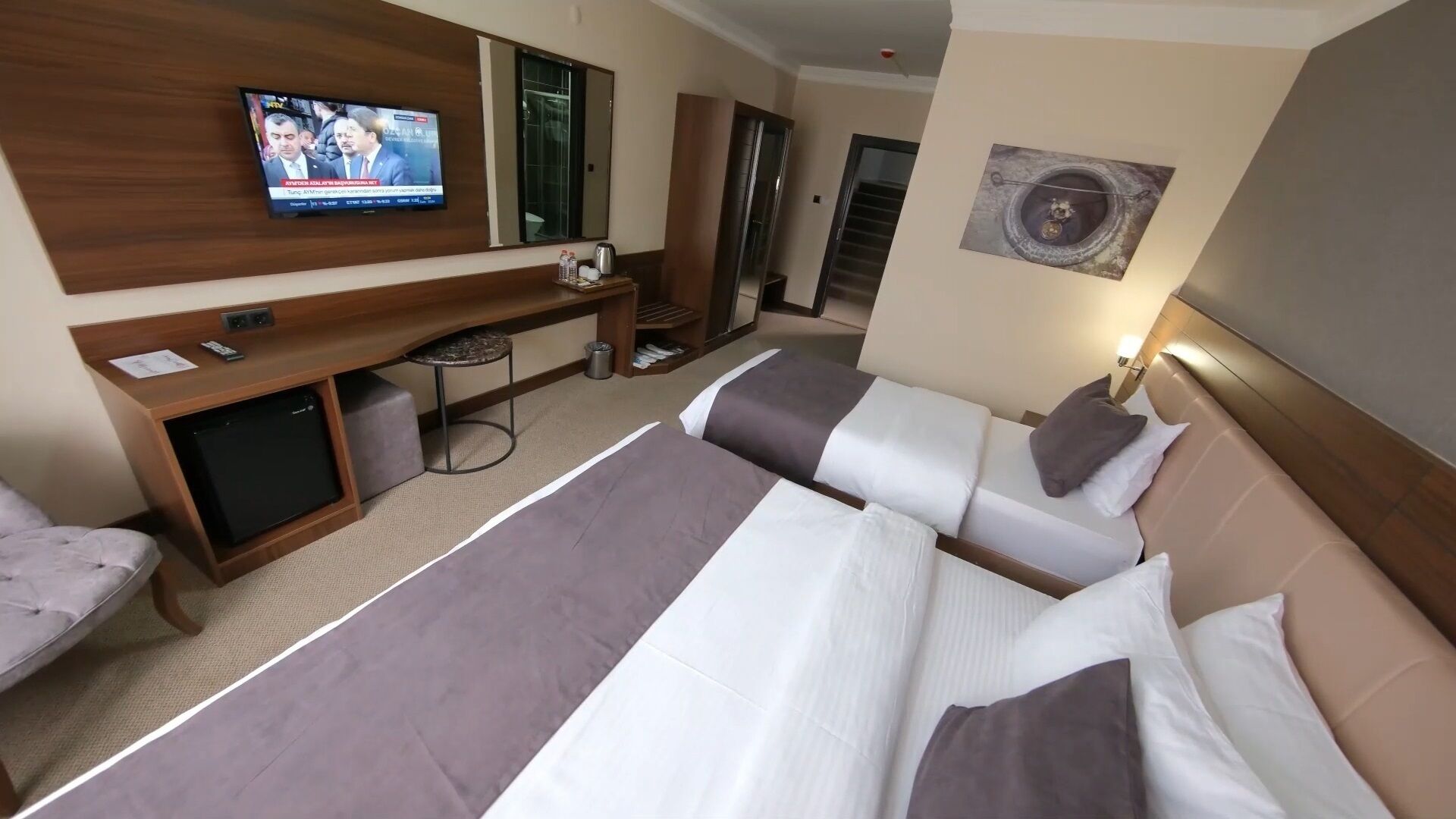 Una habitación de hotel con una cama grande, un escritorio con televisor, una mesita pequeña y una silla.