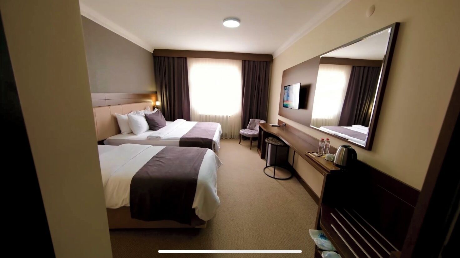 Habitación de hotel con dos camas, un escritorio, una silla, un televisor y un espejo grande.