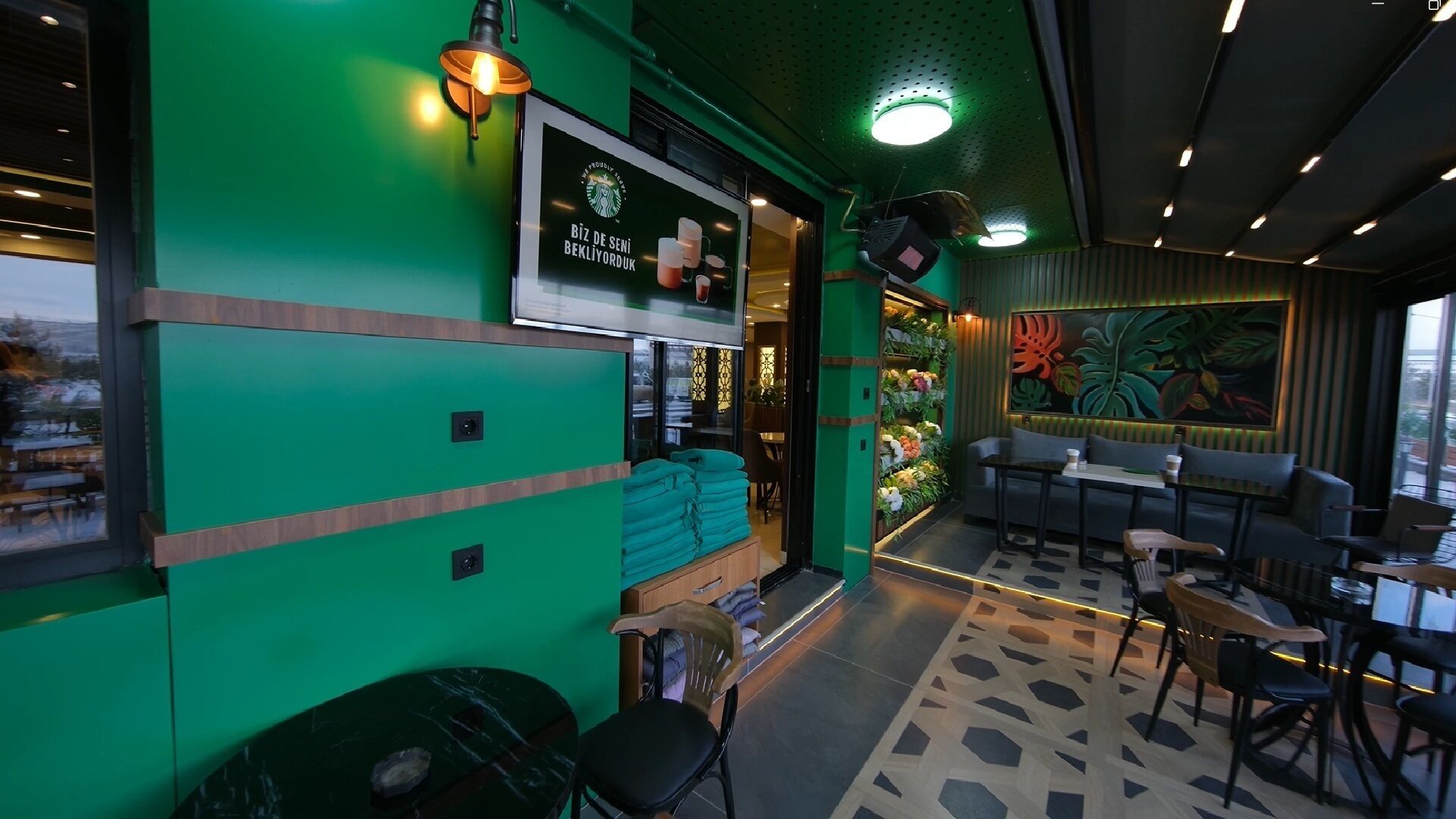 Interior de restaurante con decoración verde, zona de estar, menú colgado en la pared y una pared decorativa con plantas.