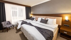 Una habitación de hotel con una cama grande, dos mesitas de noche, una silla y un ventanal con cortinas.