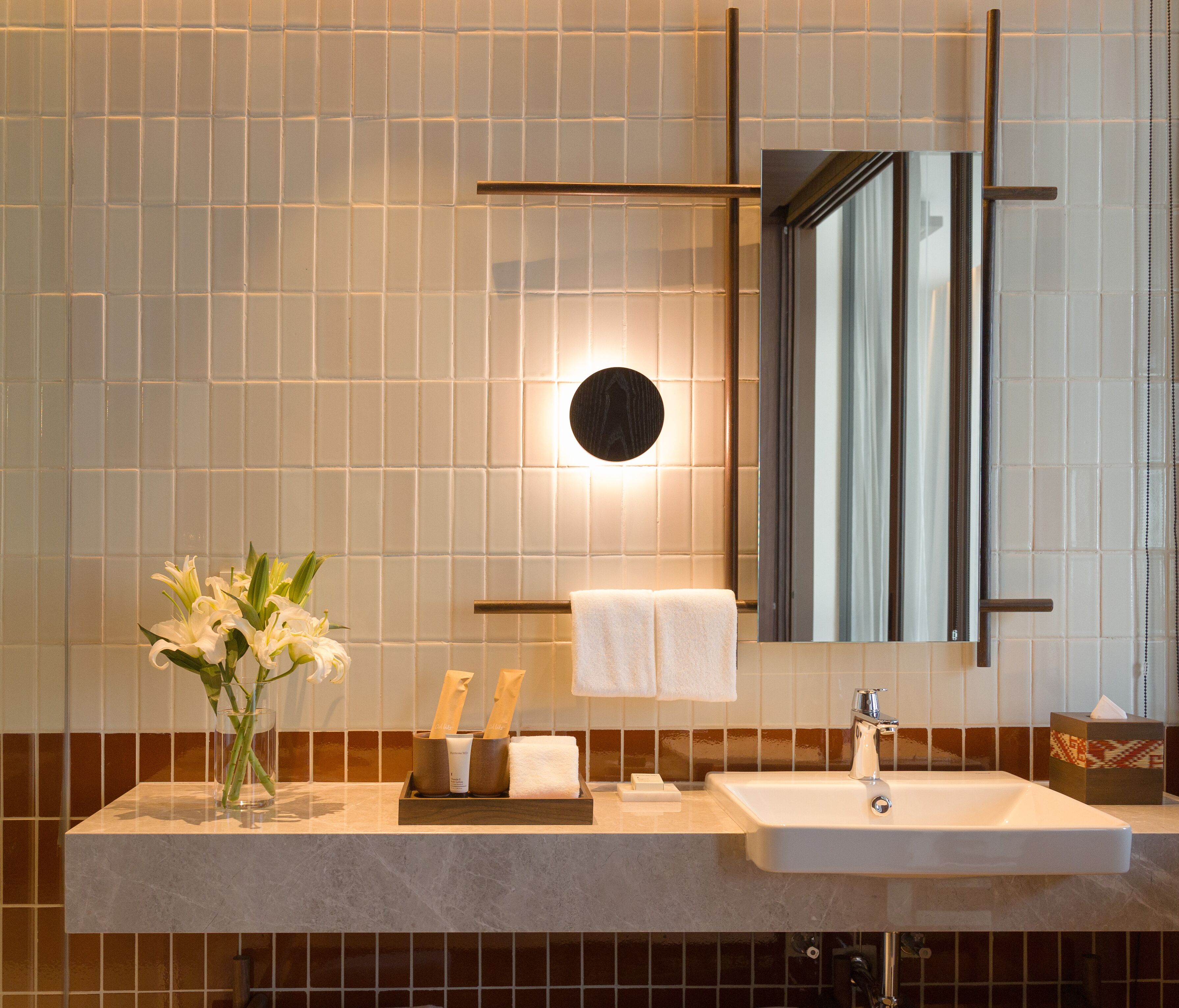 Ein modernes Badezimmer mit einem großen Spiegel, einem Waschbecken und einer Vase mit weißen Blumen.