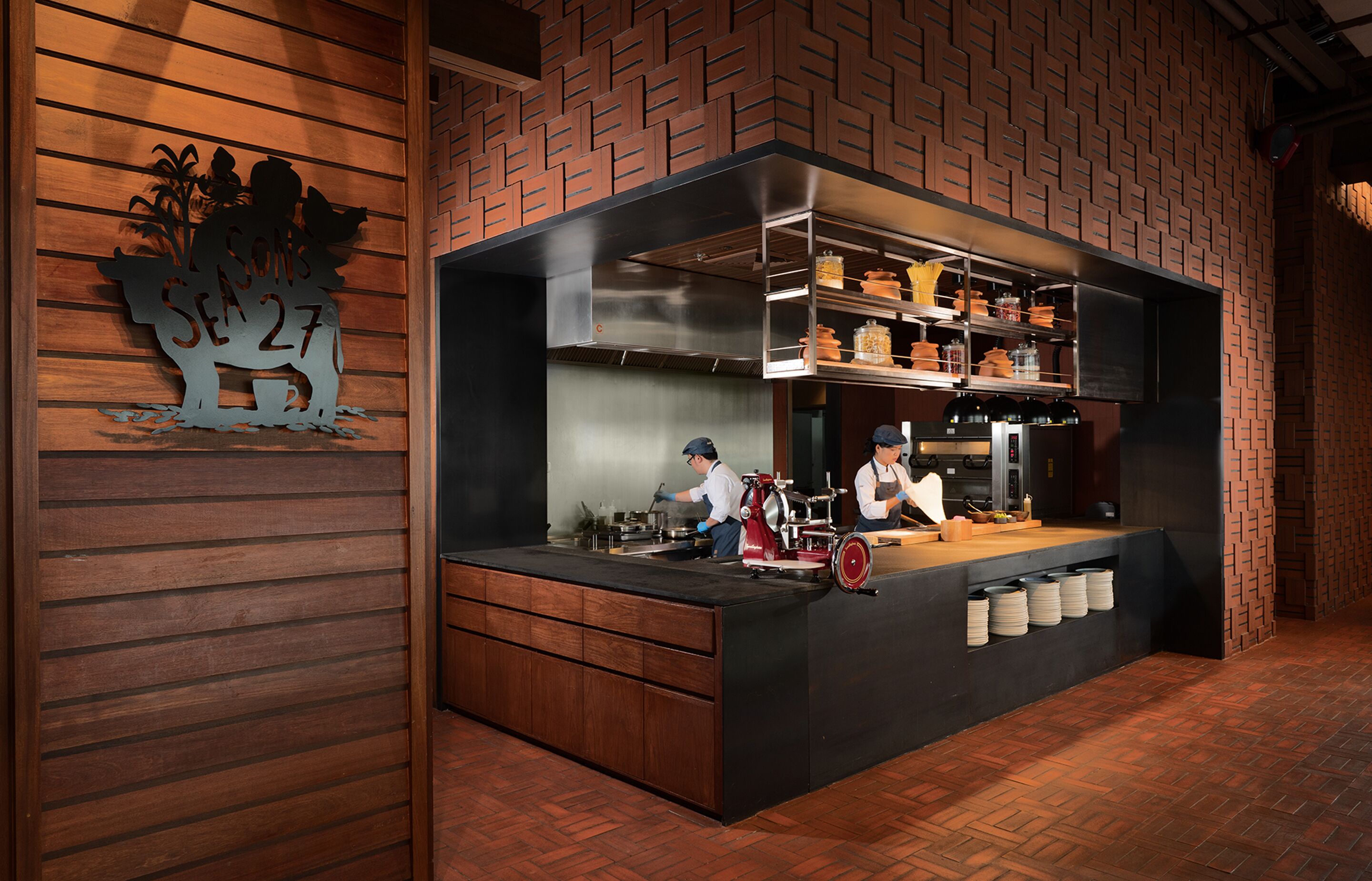 Una cocina con pared de ladrillo, paneles de madera y una isla central con dos cocineros.