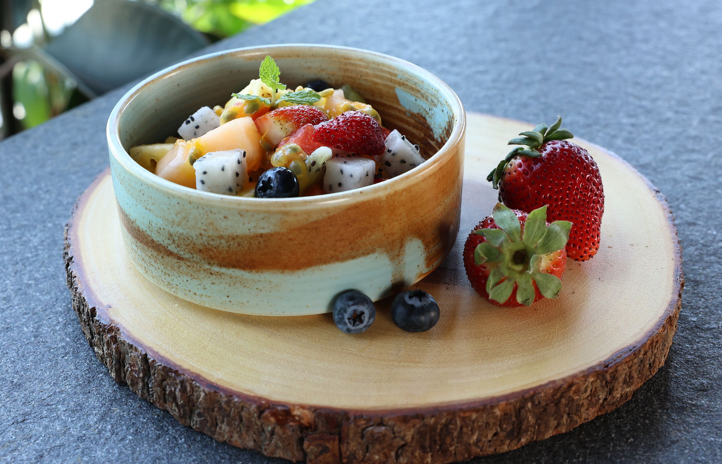 Un cuenco de ensalada de frutas sobre una tabla de madera.