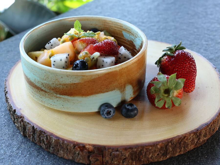 Un cuenco de ensalada de frutas sobre una tabla de madera.