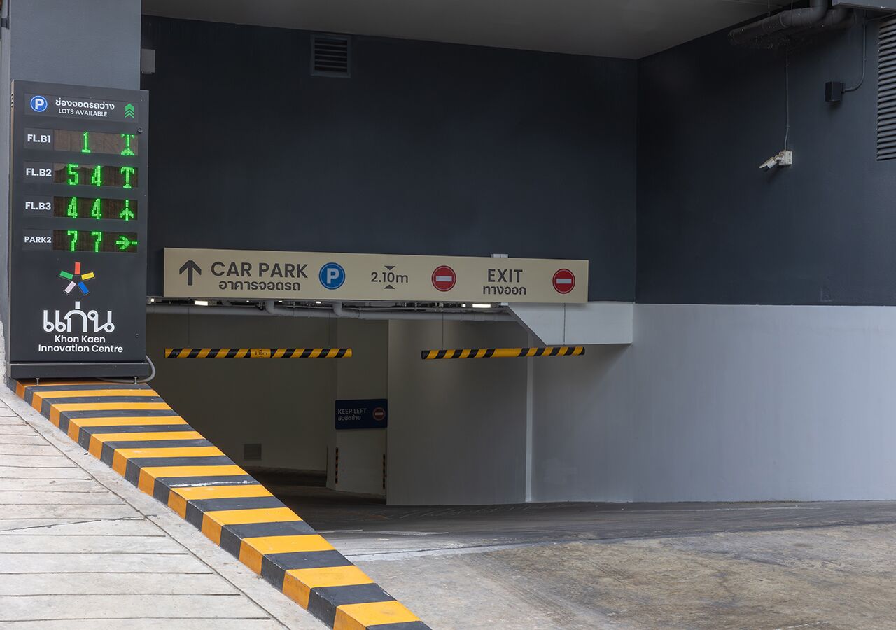 A car park with a digital sign indicating available parking spots, directional arrows for car park and exit, and a sign for the Khon Kaen Innovation Centre.