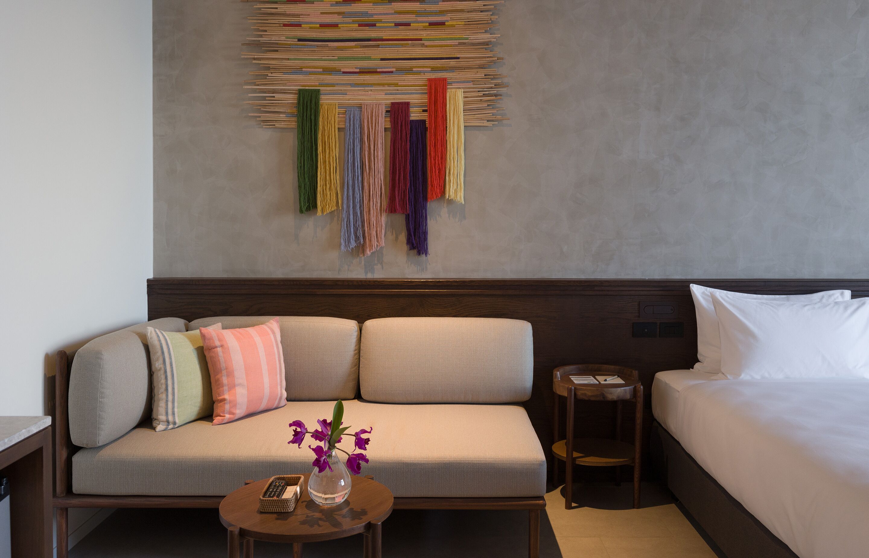 Ein Hotelzimmer mit Sofa, einem kleinen Tisch mit Blumenvase, einem Nachttisch und einem Bett.
