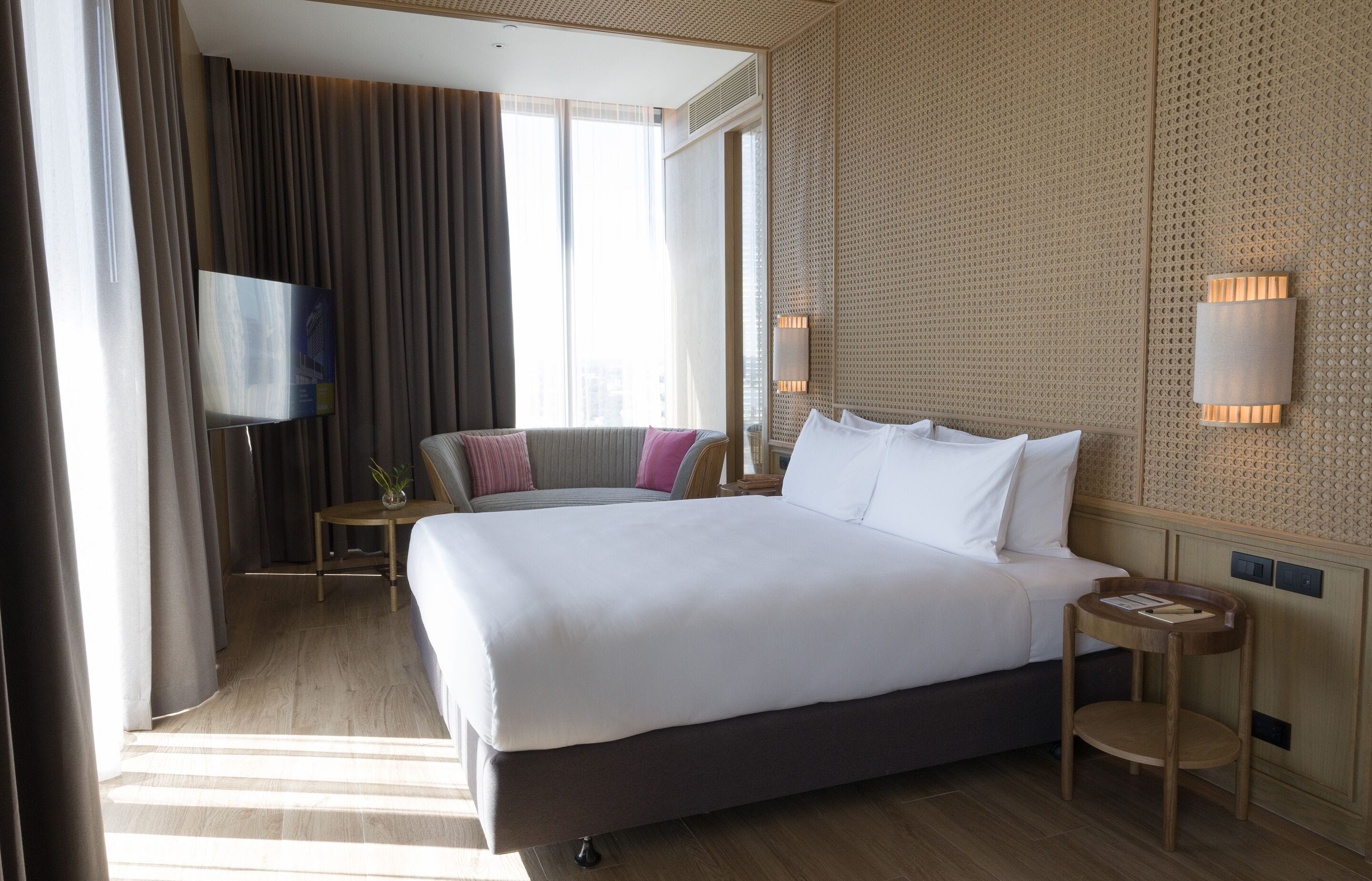 Ein Hotelzimmer mit einem großen Bett, einem Fernseher, einem kleinen Tisch und einer Wandlampe.