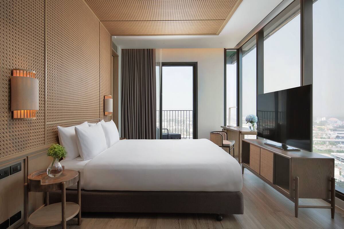 A modern hotel room with a large bed, a TV, and a view of the city.