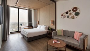 Una habitación de hotel moderna con una cama grande, un sofá, una mesa de centro y vistas a la ciudad.