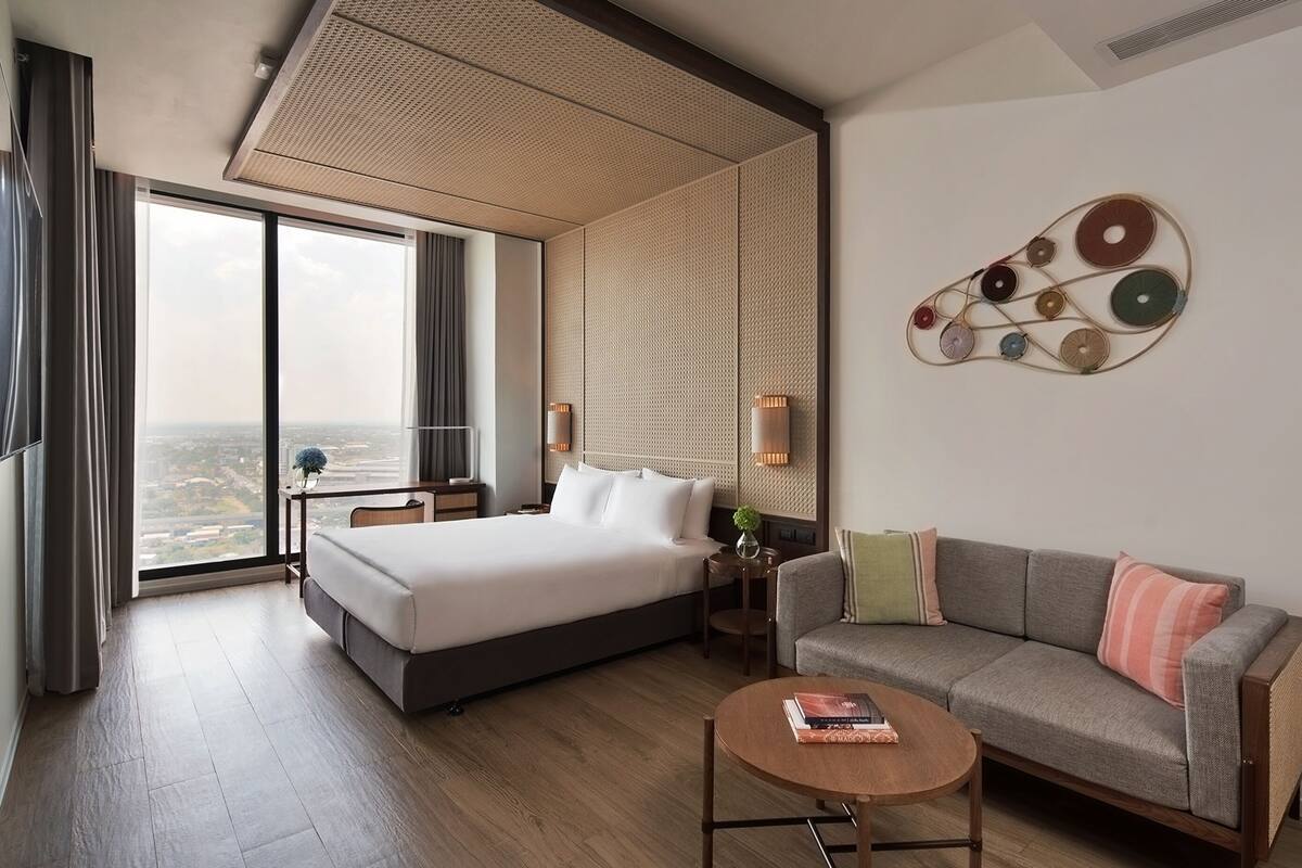 A modern hotel room with a large bed, a sofa, a coffee table, and a view of the city.