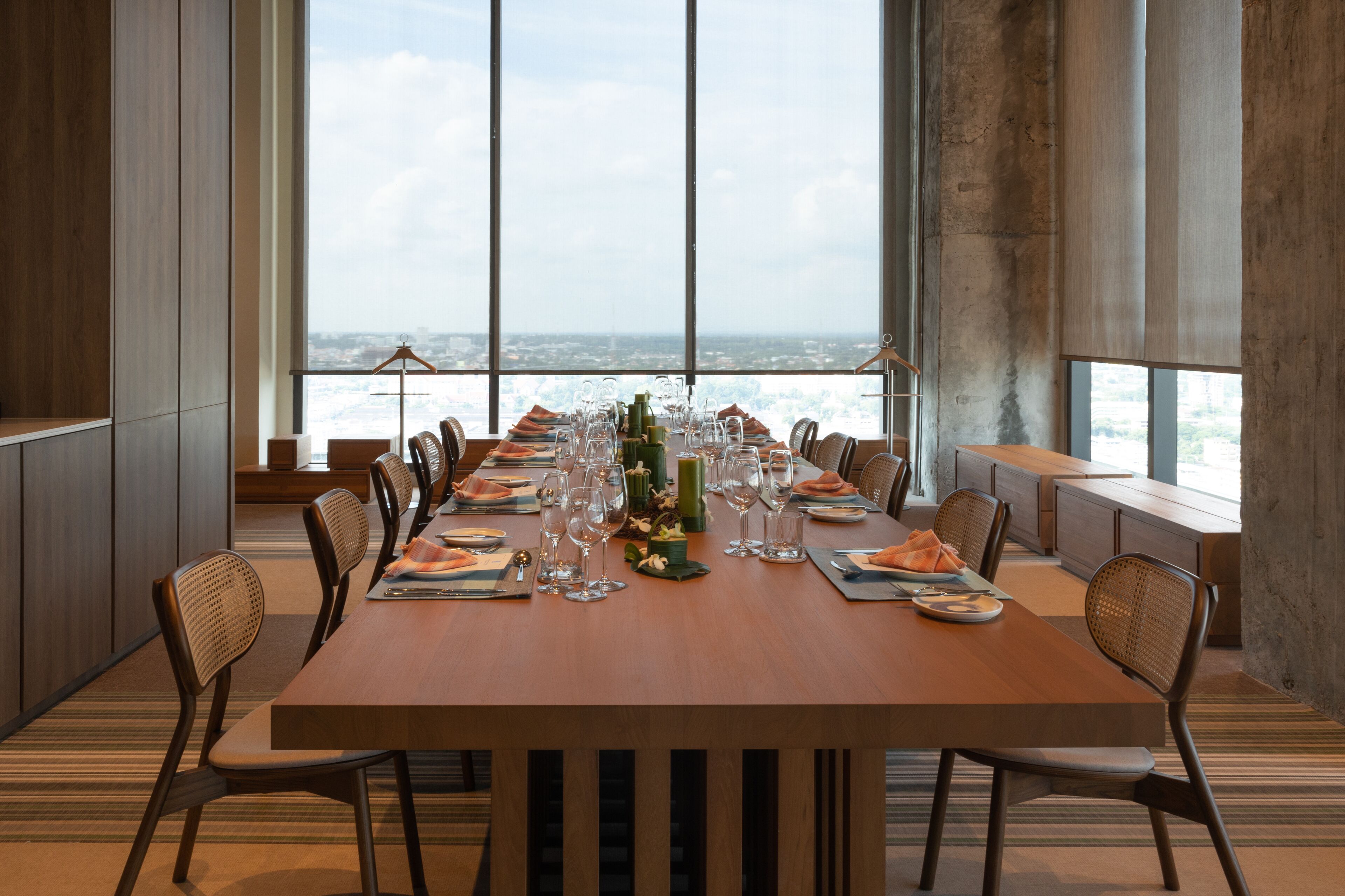 A long dining table set for a meal with chairs, a city view through large windows, and a modern interior design.