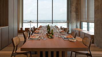 A long dining table set for a meal with chairs, a city view through large windows, and a modern interior design.