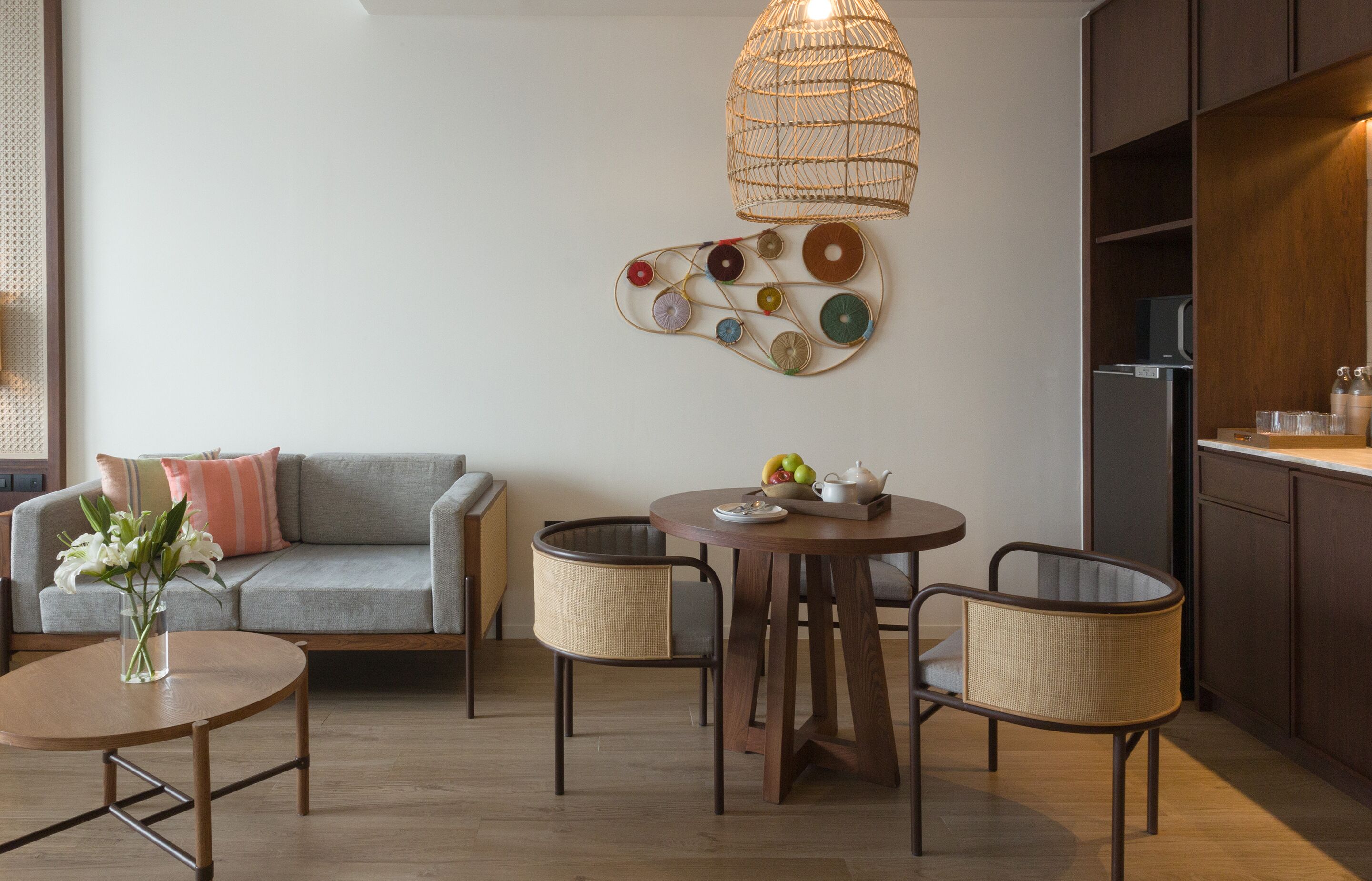 A modern living room with a grey sofa, a round wooden coffee table, wicker chairs, and a decorative wall piece.