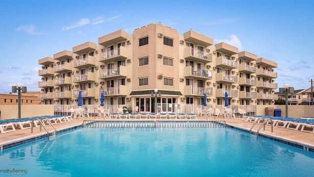 Un hotel de varios pisos con piscina, balcones y mobiliario exterior.