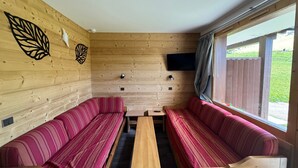A cabin interior with two striped sofas, a wooden table, and a TV mounted on the wall.