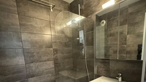 A modern bathroom with a glass-enclosed shower, a white bathtub, and a large mirror above the sink.