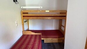 A bunk bed with a wooden frame and a red striped mattress.