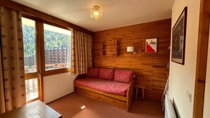 Une pièce chaleureuse avec un mur en bois, un canapé, une petite table et une fenêtre avec des rideaux.