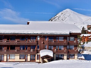 Ein mehrstöckiges Hotel mit verschneitem Dach, hölzernen Balkonen und Bergblick.