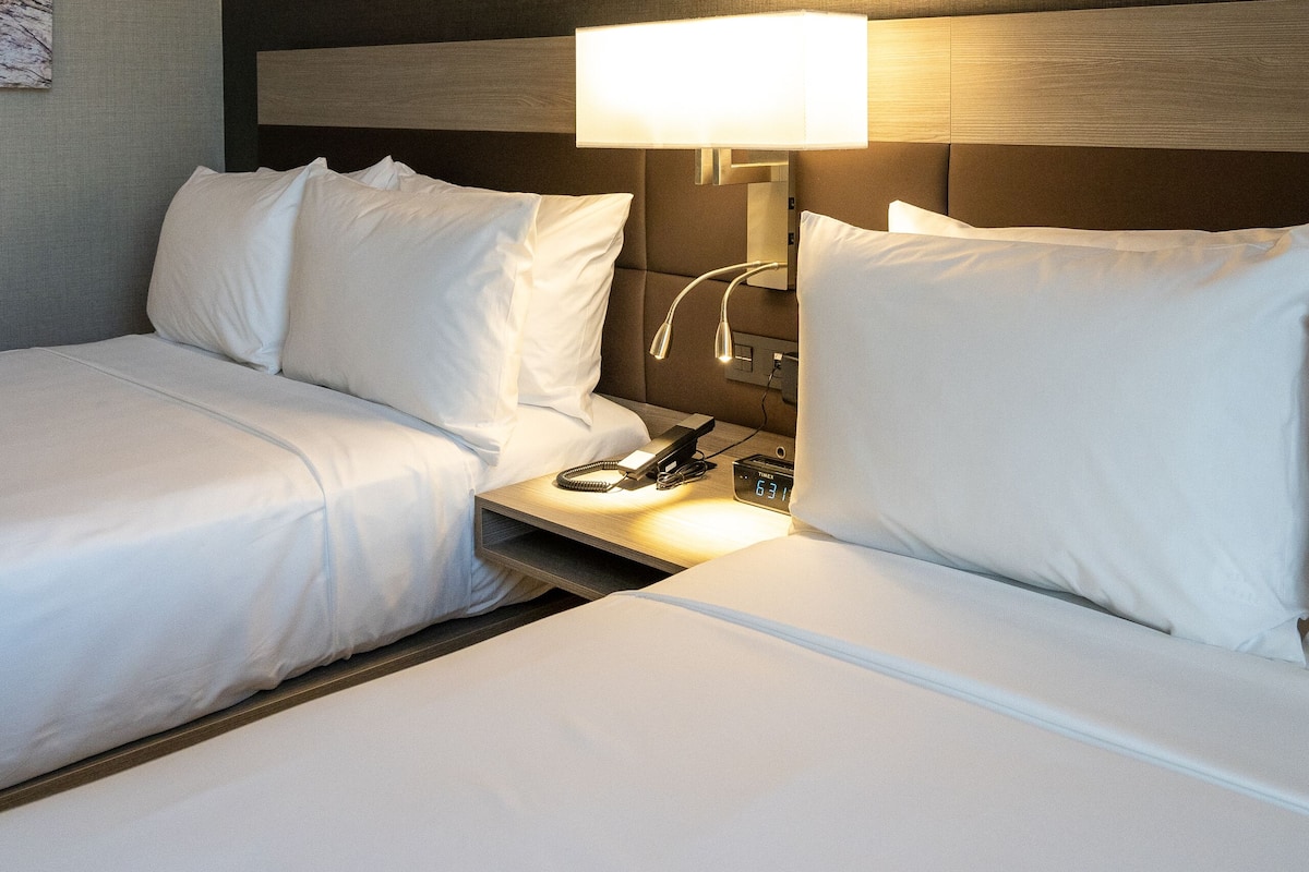 Une chambre d’hôtel avec deux lits, une table de chevet et une lampe.