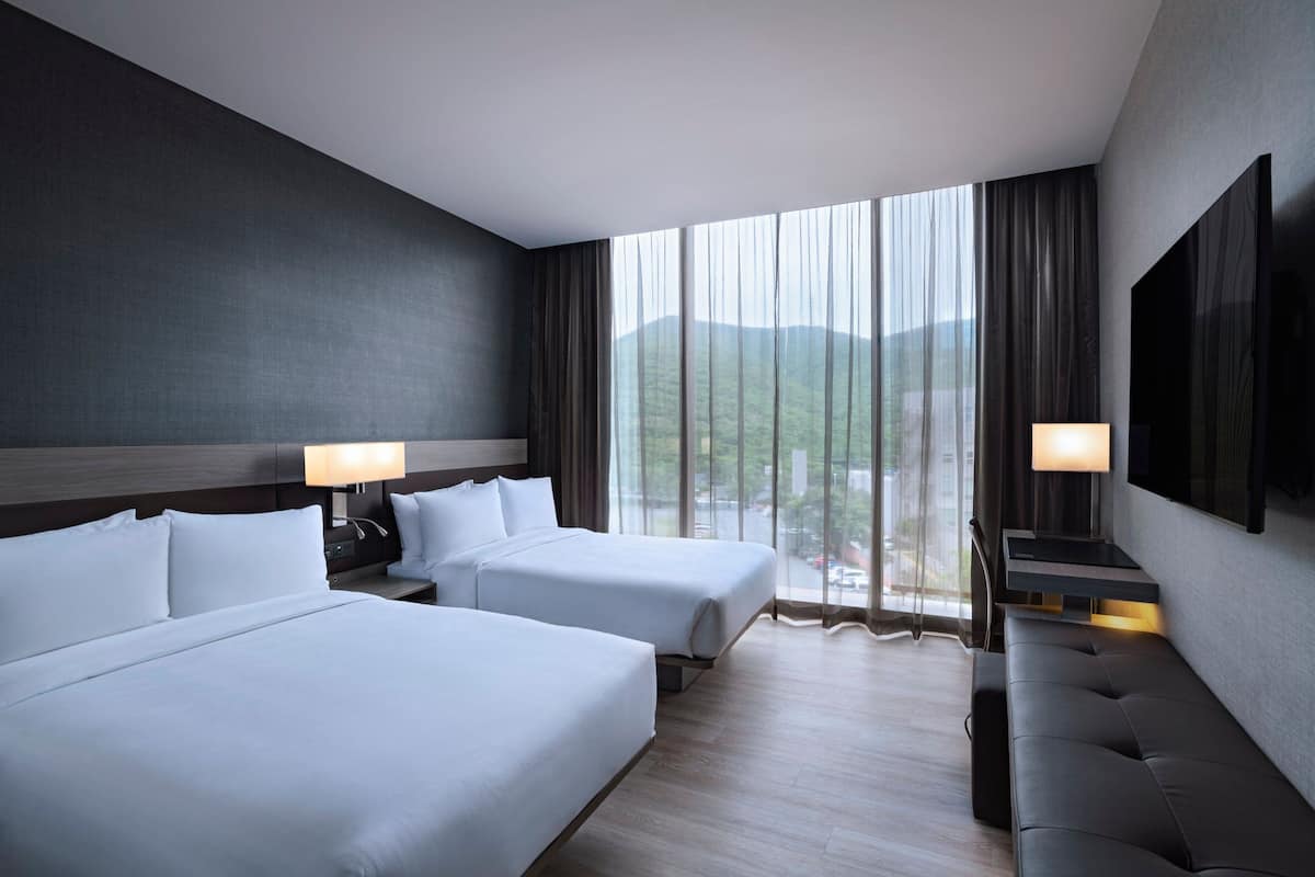 A hotel room with two beds, a sofa, a TV, and a large window with a view of mountains.