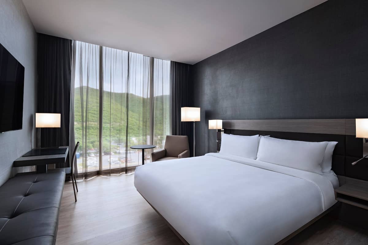 A modern hotel room with a large bed, a desk, a chair, and a small table.