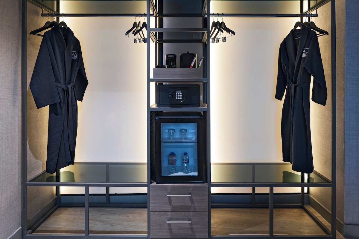 Una habitación de hotel moderna con armario empotrado que incluye dos albornoces, un microondas y un refrigerador pequeño.