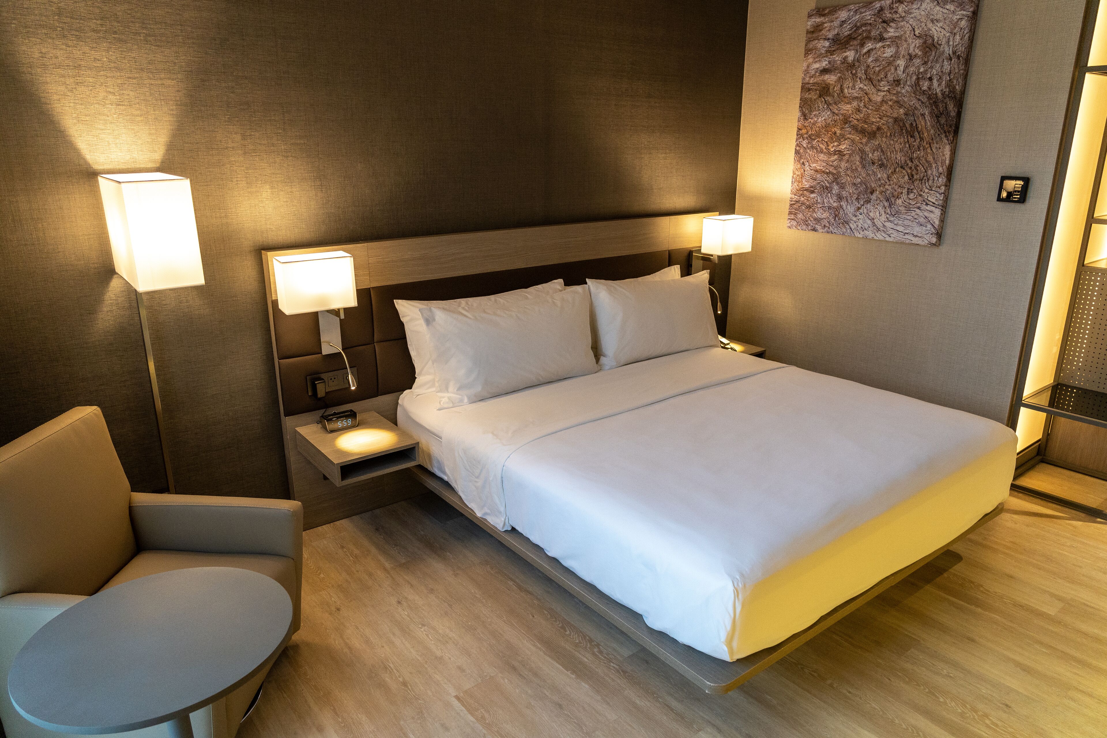 Una habitación de hotel moderna con una cama grande, lámparas de noche, una mesita y una silla.