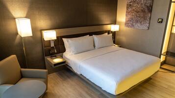 Una habitación de hotel moderna con una cama grande, lámparas de noche, una mesita y una silla.