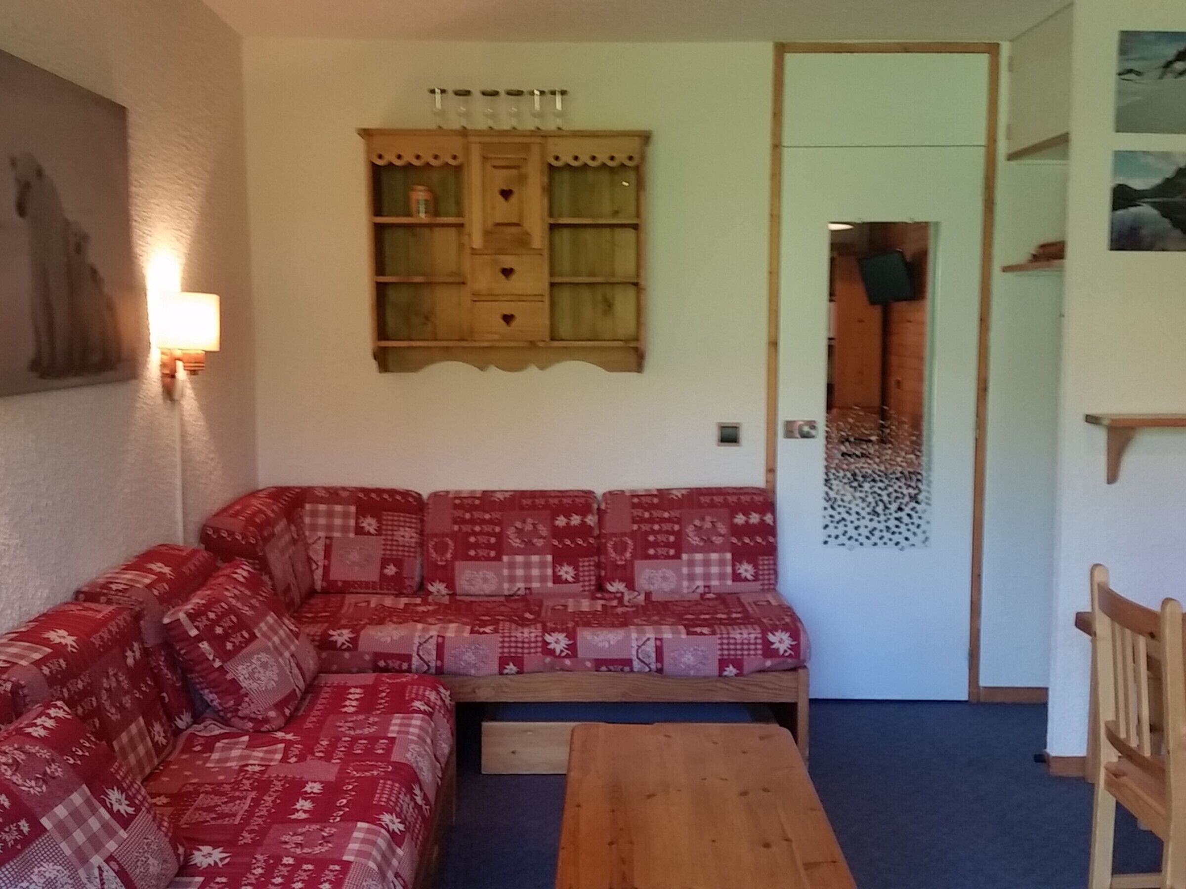 Een gezellige woonkamer met een rood gestreept bankje, een houten tafel en een wandkast.
