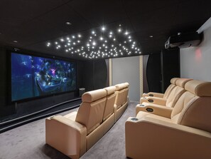 A home theater with beige leather recliners, a large flat-screen TV, and a ceiling with star-like lights.
