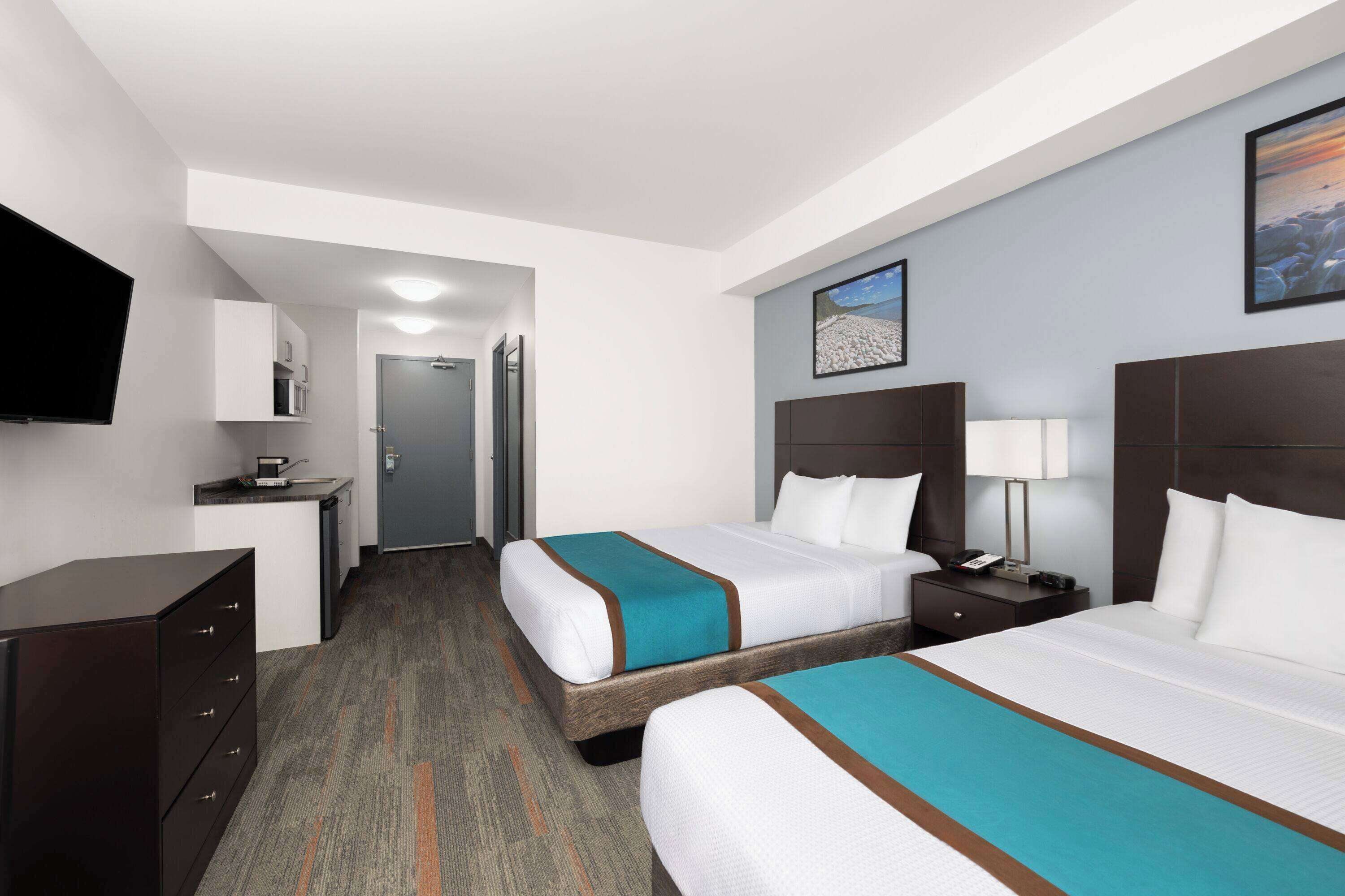 A hotel room with two beds, a TV, a desk with a microwave, and a door leading to a bathroom.