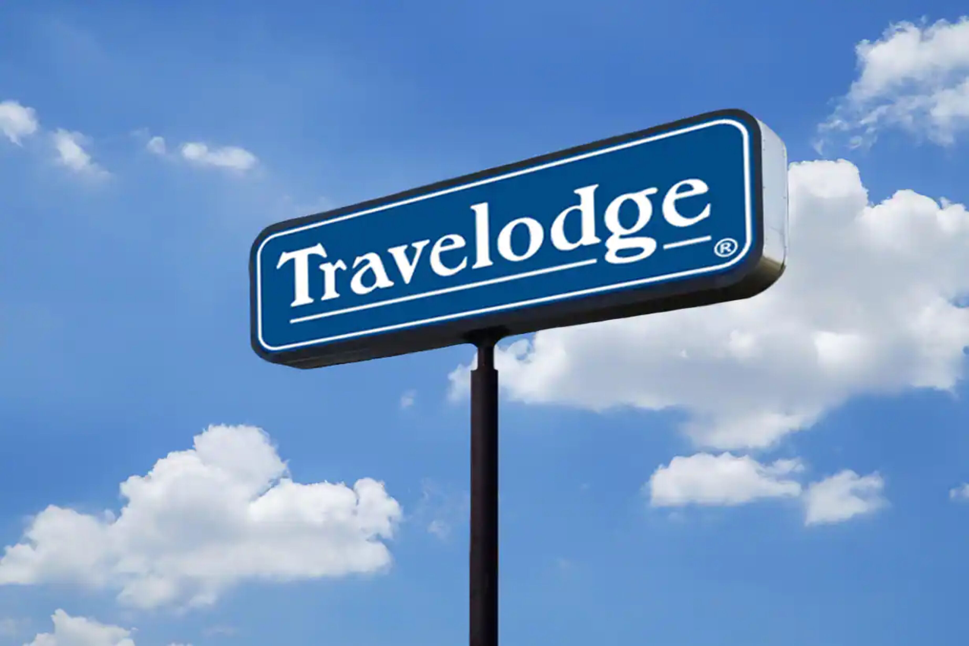 Un panneau bleu sur lequel on peut lire le mot « Travelodge », avec en arrière-plan un ciel dégagé et quelques nuages.