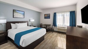 Habitació d'hotel amb un llit gran, una taula de treball, una cadira, un televisor i una finestra amb cortines.