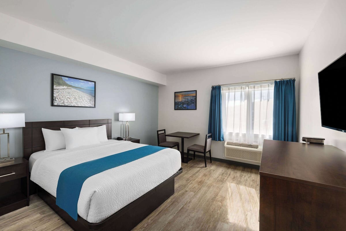 Ein Hotelzimmer mit einem großen Bett, einem Schreibtisch, einem Stuhl, einem Fernseher und einem fenster mit Vorhängen.