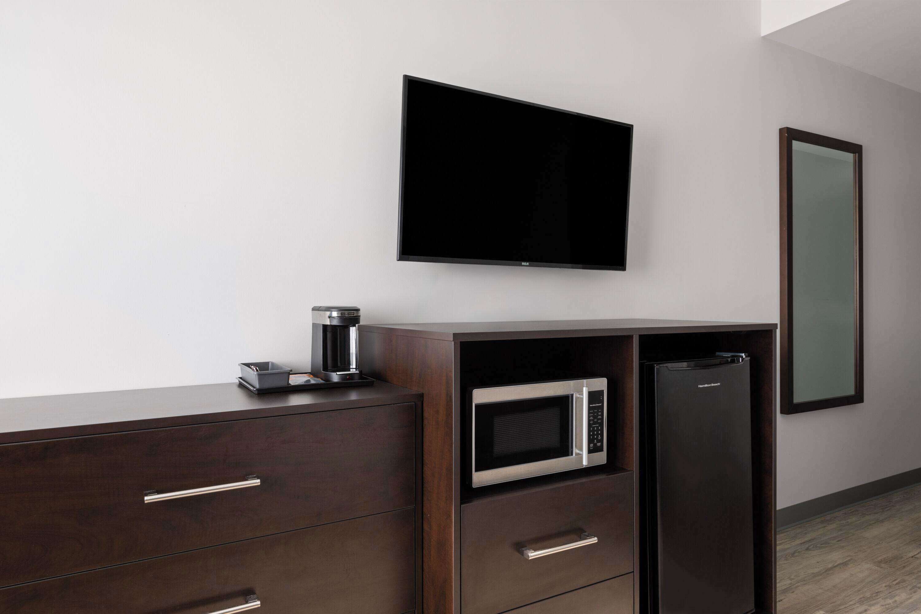 A modern kitchen with a built-in microwave and refrigerator, a coffee maker on the counter, and a flat-screen TV mounted on the wall.