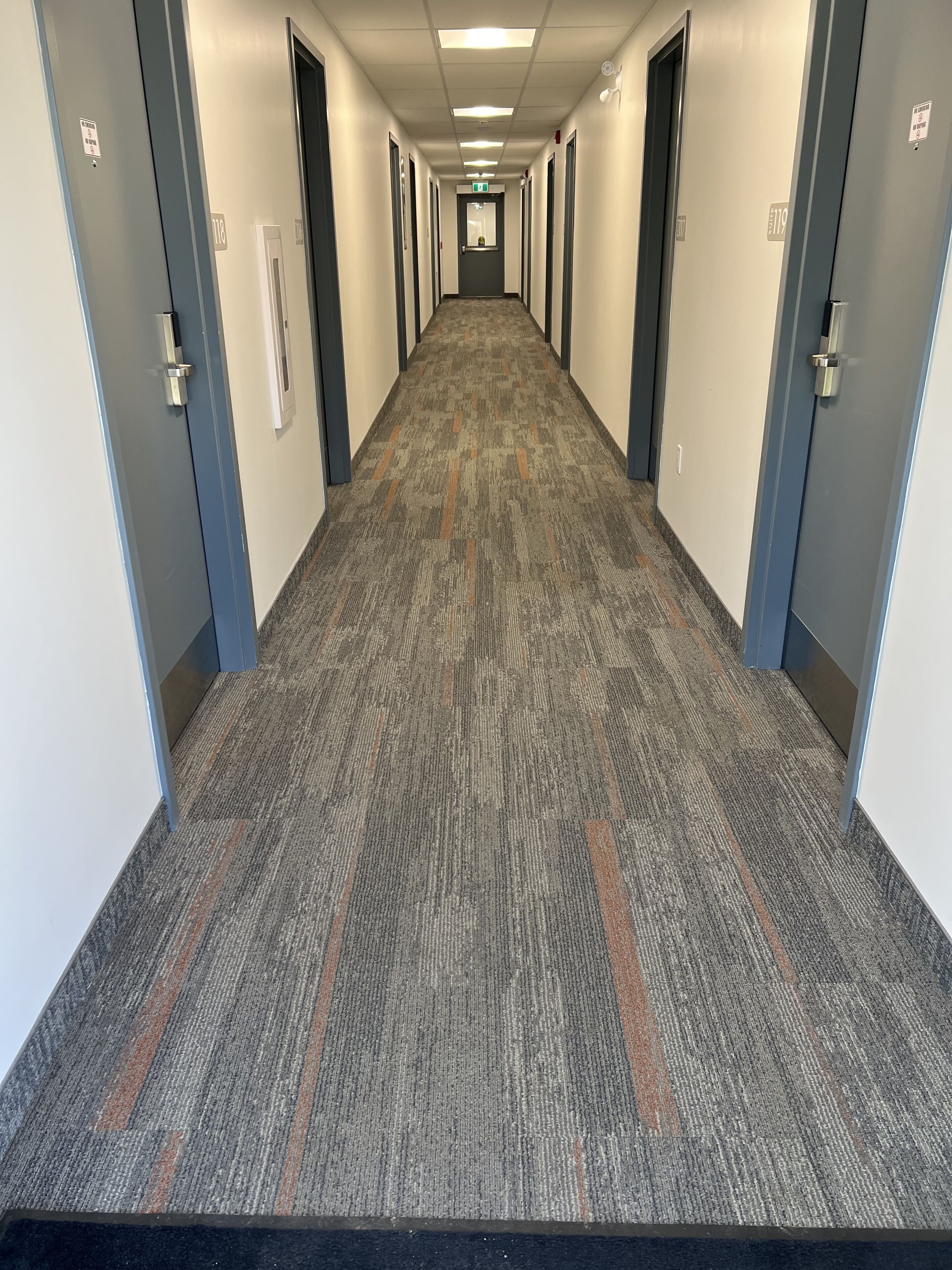 A long, narrow hallway with carpeted floors and doors on both sides, leading to individual rooms.
