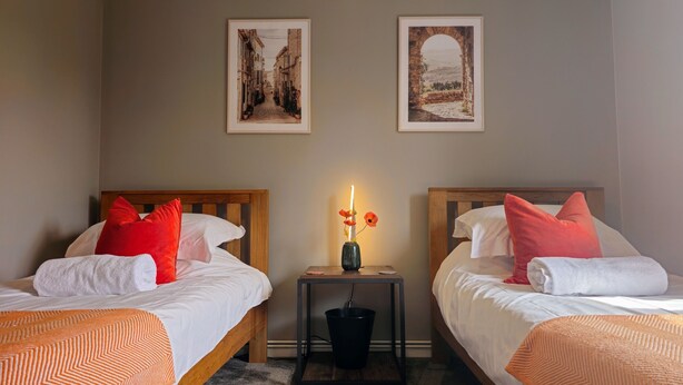 Une chambre d’hôtel avec deux lits, chacun étant agrémenté de draps blancs et d’oreillers rouges. Une petite table avec un vase de fleurs se trouve entre les deux lits.