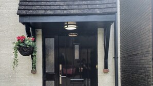 Une porte à cadre noir, ornée d’une petite fenêtre et d’un pot de fleurs suspendu.