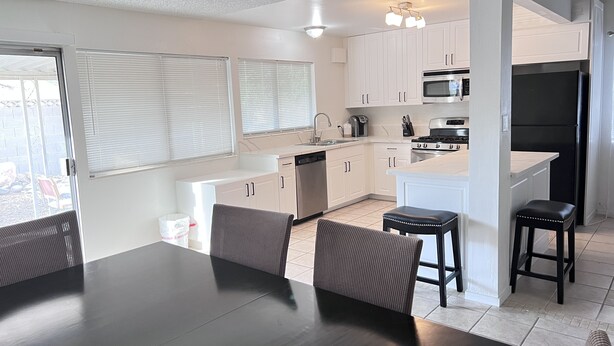 A modern kitchen with white cabinets, a black refrigerator, and a dining area with a black table and chairs. - Big monthly discount. Professional travelers,relocating or just visiting. (Henderson)