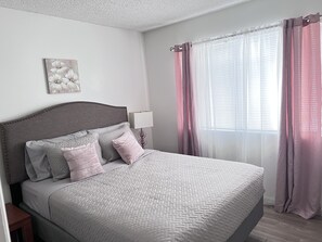 A neatly made bed with a grey headboard, a bedside lamp, and a floral artwork on the wall. - Big monthly discount. Professional travelers,relocating or just visiting. (Henderson)