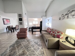 A living room with a sofa, armchair, coffee table, and a foosball table. There is a dining area with chairs and a table, and a kitchen in the background. - Big monthly discount. Professional travelers,relocating or just visiting. (Henderson)