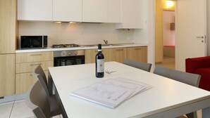 Una cocina moderna con armarios blancos, un microondas, una estufa a gas y una botella de vino sobre la mesa.