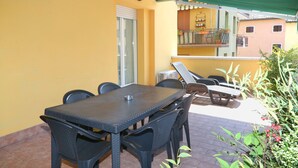 Un patio con una mesa, sillas, un ventanal y un balcón con plantas.