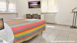 Habitación de hotel con cama, escritorio, silla, radiador y ventana con cortinas.