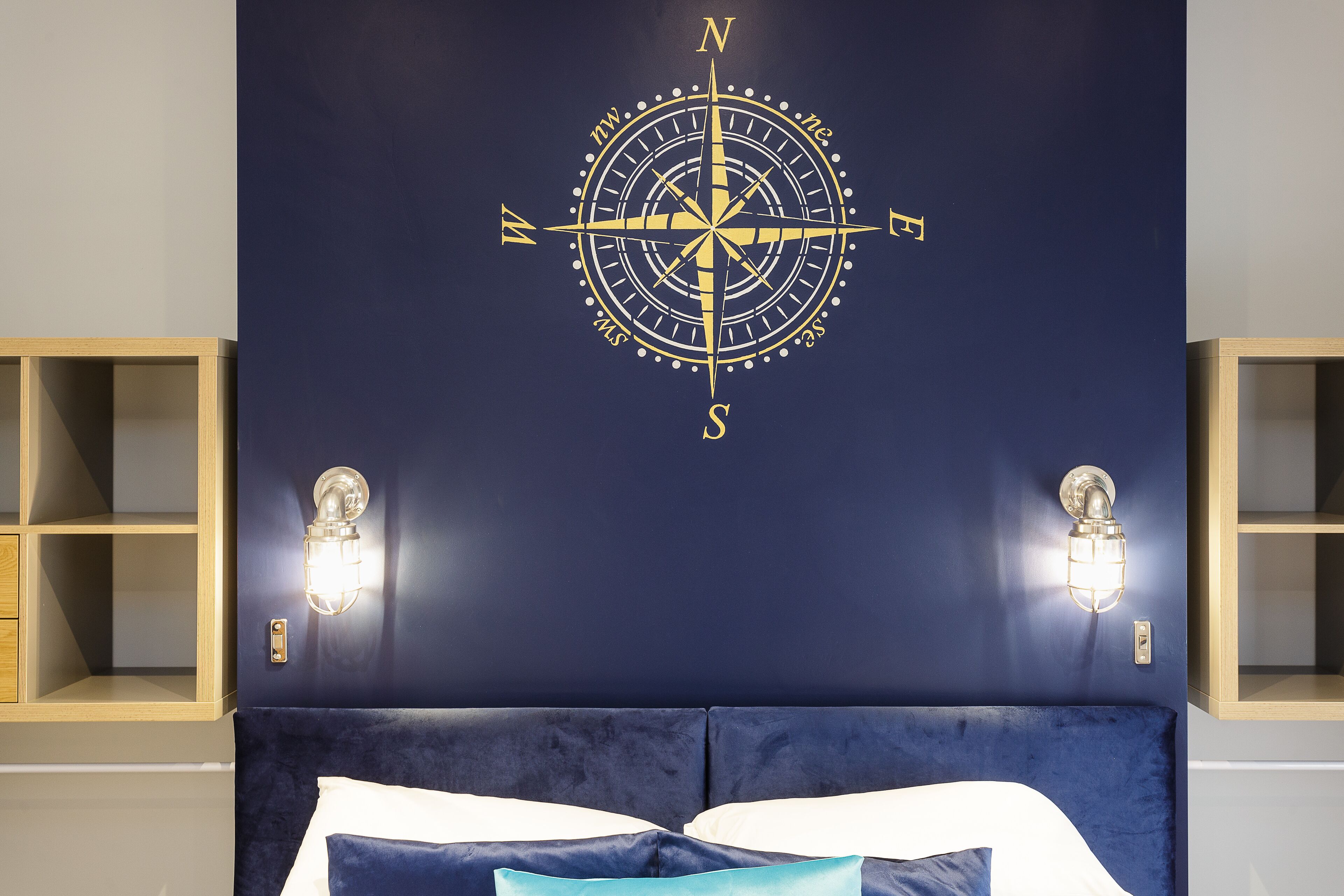 A room with a large compass wall decoration, a bed with white and blue bedding, and two wall-mounted light fixtures.